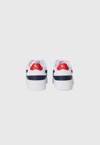 Sneakers bianche con accenti blu navy e linguette rosse sul tallone. Presentano un materiale texture, collo imbottito e un logo visibile sul tallone.