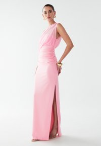 Růžové šaty na jedno rameno s nařasením v pase a rozparkem až k stehnům. Vyrobené z hladkého materiálu s přiléhavým střihem.