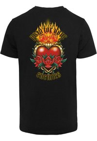 Black t-shirt featuring a vibrant design: a red heart with flames, surrounded by roses and the text "pray for your enemies" in yellow.