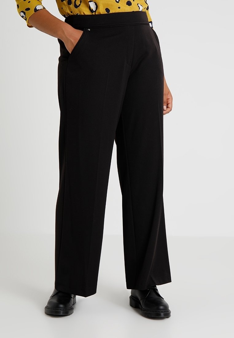 Pantalon large noir avec une texture lisse, taille élastique et poches latérales. Associé à un haut jaune à motifs.