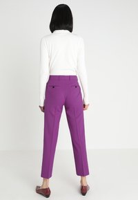 Lila skräddarsydda byxor med rak benprofil, med dubbla bakfickor och en slät tygtextur, matchade med en vit långärmad topp.