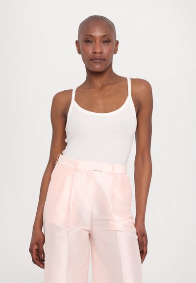 White tank top with thin straps, paired with light pink satin wide-leg trousers, featuring side pockets and a smooth texture.