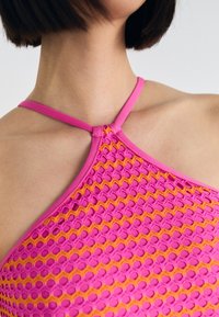 Růžový a oranžový síťový top s výrazným vzorem. Má tenké ramínka a jedinečný uzlový detail v oblasti límce.