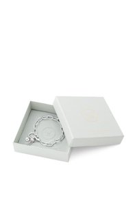 Söljkedjearmband i en ljusgrå låda, som har en hängande charm med en glittrande detalj och logotags. Lådan har en texturerad yta.