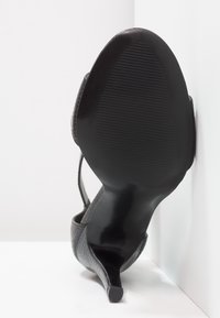 Escarpin noir à talon haut avec un dessus texturé au motif reptilien et une semelle lisse à stries. Silhouette angulaire et design à bout pointu.