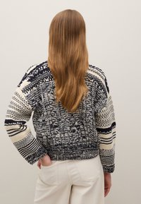 Marineblauer und cremefarbener Pullover mit Strickmuster, strukturiertem Design, weitem Ärmelschnitt und kurzem Schnitt, der einen kontrastierenden Abschlussbund zeigt.