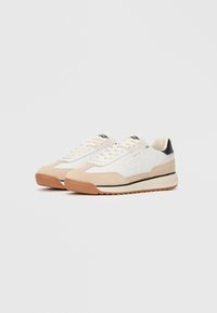 Sneakers con una parte superiore in pelle bianca, accenti in suede beige a contrasto, linguetta nera sul tallone e una suola in gomma naturale texturizzata.