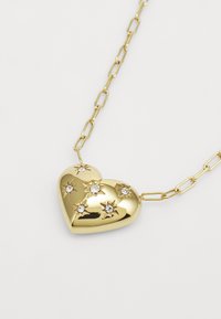 Collier en pendentif cœur doré avec des embellissements en forme d'étoile en relief et des pierres claires, suspendu à une chaîne dorée comportant des maillons allongés.
