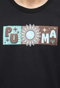 Μαύρο πουκάμισο με πολύχρωμο γραφικό που δείχνει τη λέξη "PUMA" με κεφαλαία γράμματα γύρω από ένα ηλιακό σχέδιο, με το λογότυπο Puma στο κέντρο.