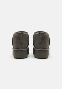 Stivali ankle in suede grigio con una spessa suola a piattaforma, dotati di fodera imbottita e linguette posteriori per una facile calzata. Cuciture dettagliate lungo le cuciture.