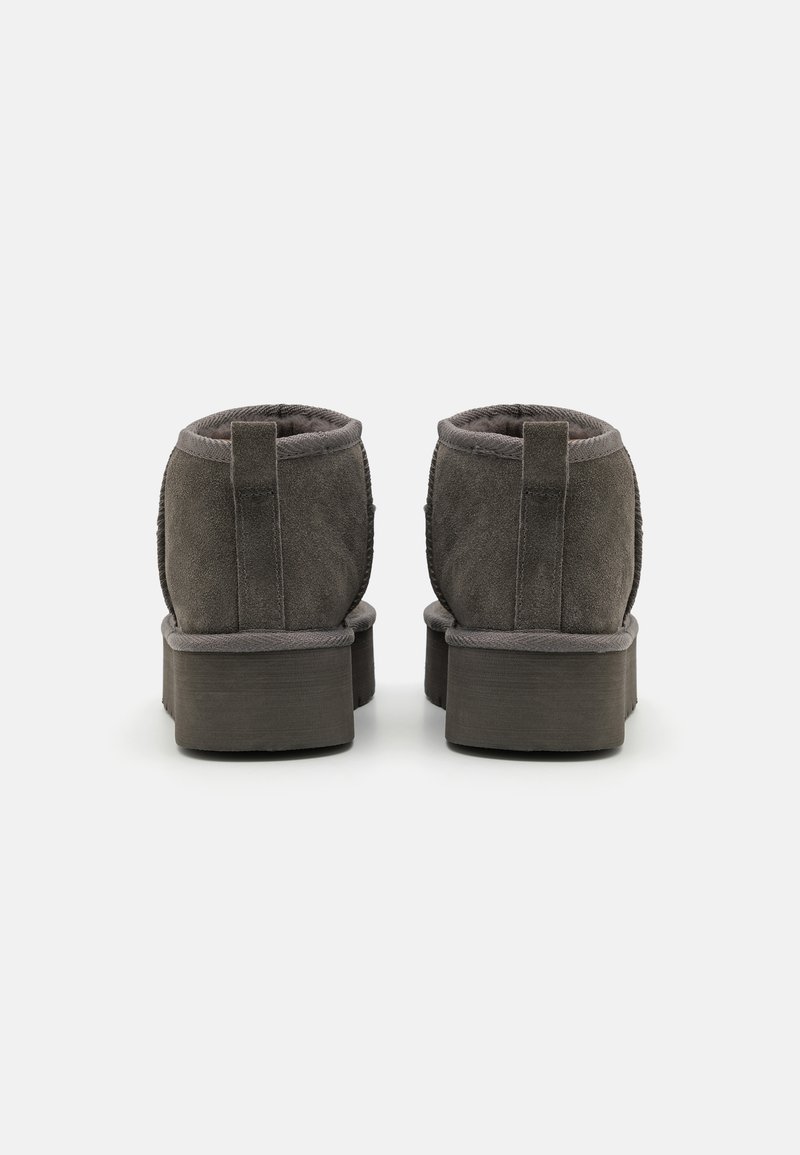 Graue Wildleder-Stiefeletten mit einer dicken Plattformsohle, ausgestattet mit gepolsterter Innenausstattung und Hinterfangschlaufen für ein einfaches Anziehen. Detaillierte Nähte entlang der Nähte.