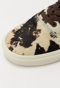 Sneaker featuring a cowhide print in black and cream with a textured finish, brown laces, and a textured rubber sole.