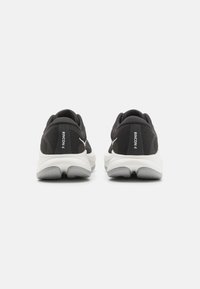 Sorte joggesko med mesh-stoff, hvite såler og hældemping. Har merkevarelogo og teksturerte detaljer på overdelen.