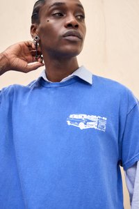 Sinine üle suurus T-särk, mis on valmistatud puuvillast, ja sellel on rinnaosas valge autode graafika. Seljas on triibuline kaelusega särk.