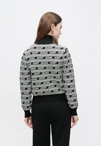 Black and white sweater with repeating "JOOP! JEANS" text pattern. Features a high neck and ribbed cuffs and hem. Fitted cropped design.