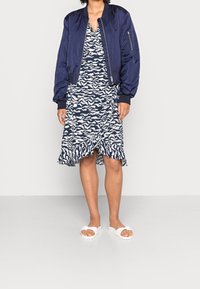 Chaqueta bomber de la marina sobre un vestido blanco y azul con un estampado y un dobladillo con volantes, combinado con sandalias de plataforma blancas.