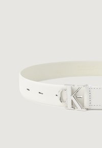 Hvit lærbelte med en sølvfarget CK-logo i metall som spenne, med jevnt fordelte hull langsremmen for justerbar størrelse.