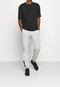 Černé bavlněné tričko s volným střihem, doplněné šedými tepláky s bočními kapsami a logy. Celkový vzhled dotváří černé boty.