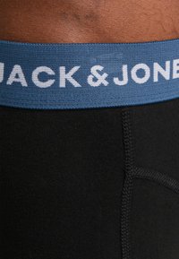 Schwarze Baumwoll-Boxershorts mit einem blauen elastischen Bund, auf dem in weißen Buchstaben "JACK & JONES" steht, sowie sichtbaren Nähdetails.