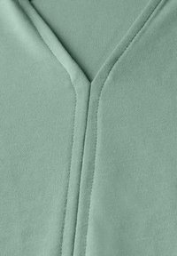 V-Ausschnitt-Oberteil aus sanftem mintgrünen Stoff, mit einer glatten Textur und dezenter Stickdetails entlang des Ausschnitts.