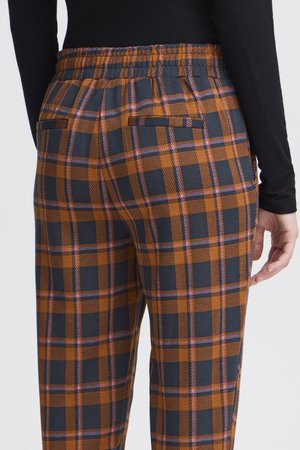 Person wearing elastic waist brown and black checkered pants with pink accents and a black long-sleeve top, shown from the back.