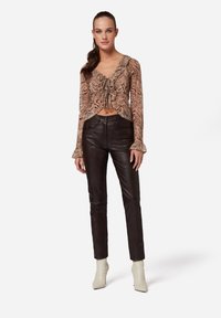 Bruine dierenprint crop blouse met strikdetail; gecombineerd met hoogwaist zwarte leren broek en crèmekleurige enkel laarzen. Getextureerde materialen zichtbaar.