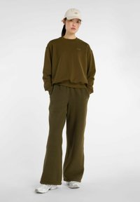 Sudadera de forro polar verde oliva y pantalones de pierna ancha a juego. El conjunto incluye una sudadera con cuello redondo y logotipo, combinada con una gorra beige.