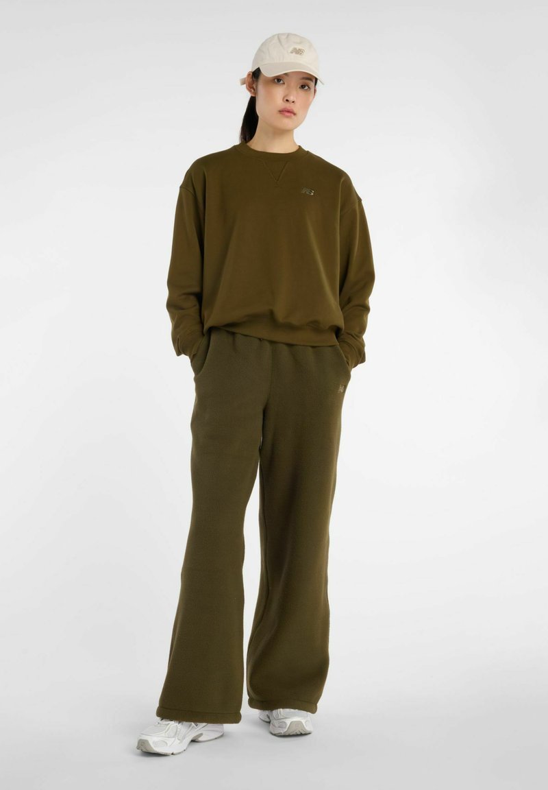 Sudadera de forro polar verde oliva y pantalones de pierna ancha a juego. El conjunto incluye una sudadera con cuello redondo y logotipo, combinada con una gorra beige.