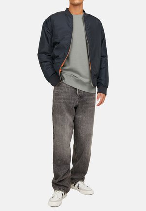 Navy bomber jacket with an orange lining, grey sweatshirt, faded black jeans, and white sneakers with black accents. Casual fit, textured materials.