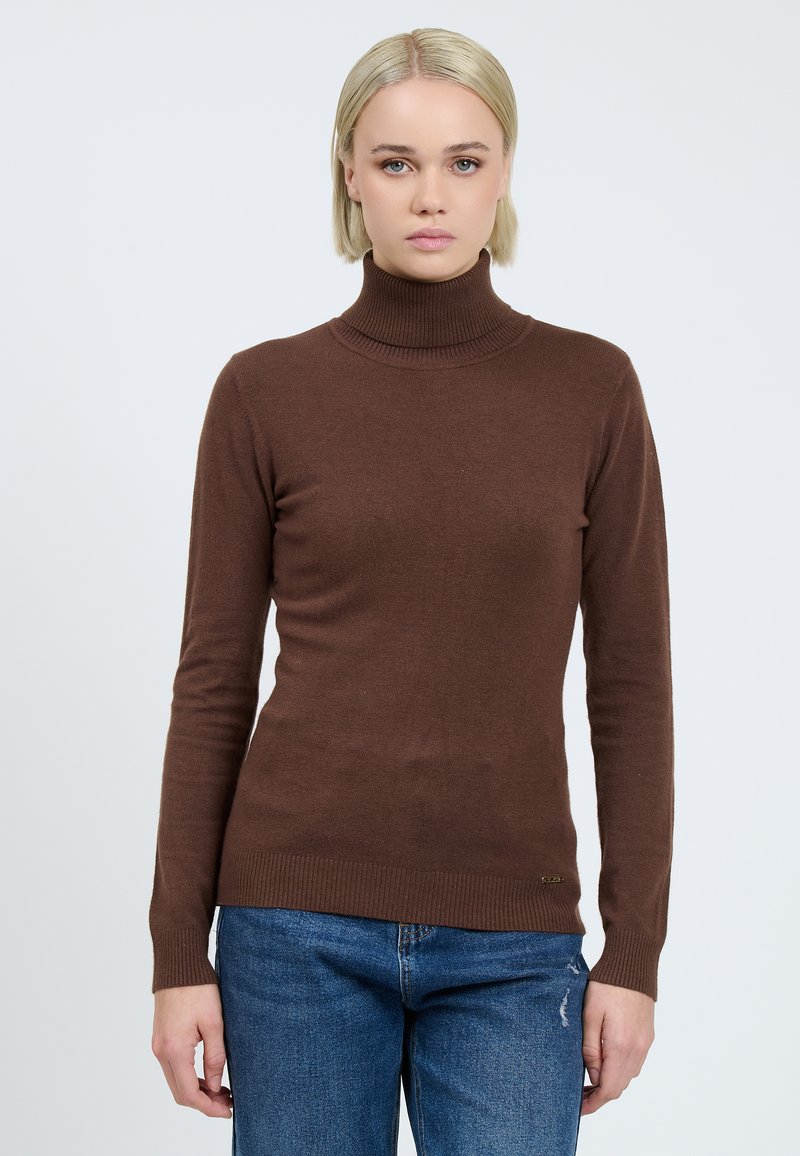 Brauner Rollkragenpullover aus weichem Stoff, mit langen Ärmeln und gerippten Abschlüssen. Getragen mit blauen Jeans.