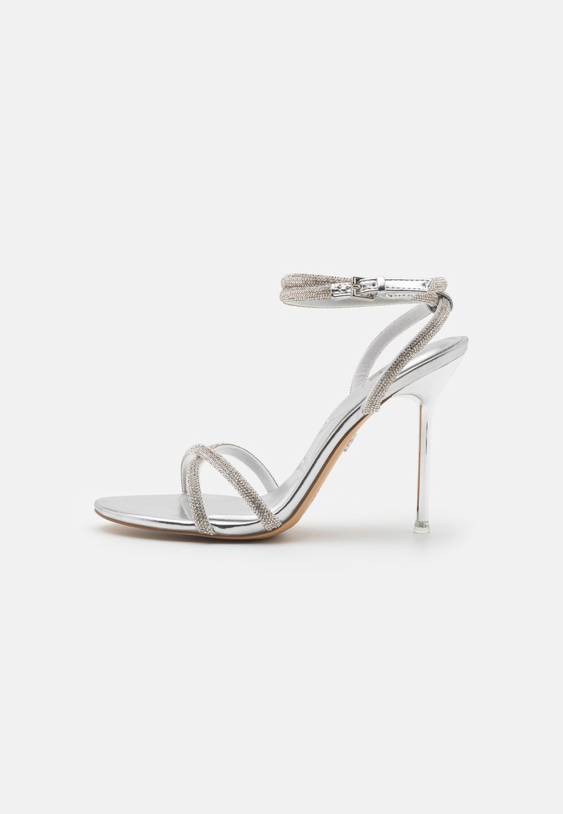 Silberne High-Heels Sandale mit einem eleganten Design, ausgestattet mit metallischen Riemen und einem transparenten Knöchelriemen. Glatte metallische Oberfläche.