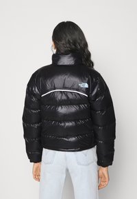 Black puffer jacket with a shiny finish, tall collar, and a white accent stripe across the back. Features a logo on the left shoulder.