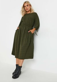 Vihreä ruudullinen mekko, jossa on kolme neljänneshihaa, kireä vyötärö, sivutaskut ja keskipitkä pituus. Yhdistetty mustiin nauhakengät.