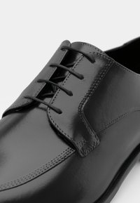 Black leather dress shoe with smooth, glossy finish. Features a six-eyelet lacing system and subtle stitching along the edges.