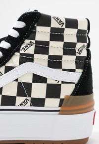 Zapatillas altas en un patrón de cuadros en blanco y negro, con acentos en cuero blanco y una suela de goma marrón, que presentan materiales texturizados.