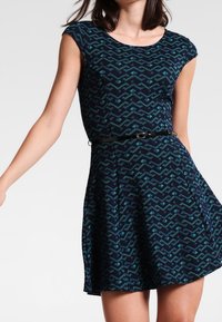 Sukienka z krótkim rękawem w granatowym kolorze z fakturowanym wzorem zygzakowatym w zielonym odcieniu. Posiada dopasowaną talię z cienkim paskiem oraz rozkloszowaną spódnicę.