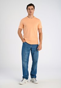T-shirt a girocollo arancione chiaro con maniche corte, abbinato a jeans blu dritti e scarpe da ginnastica bianche. Design semplice e minimal.