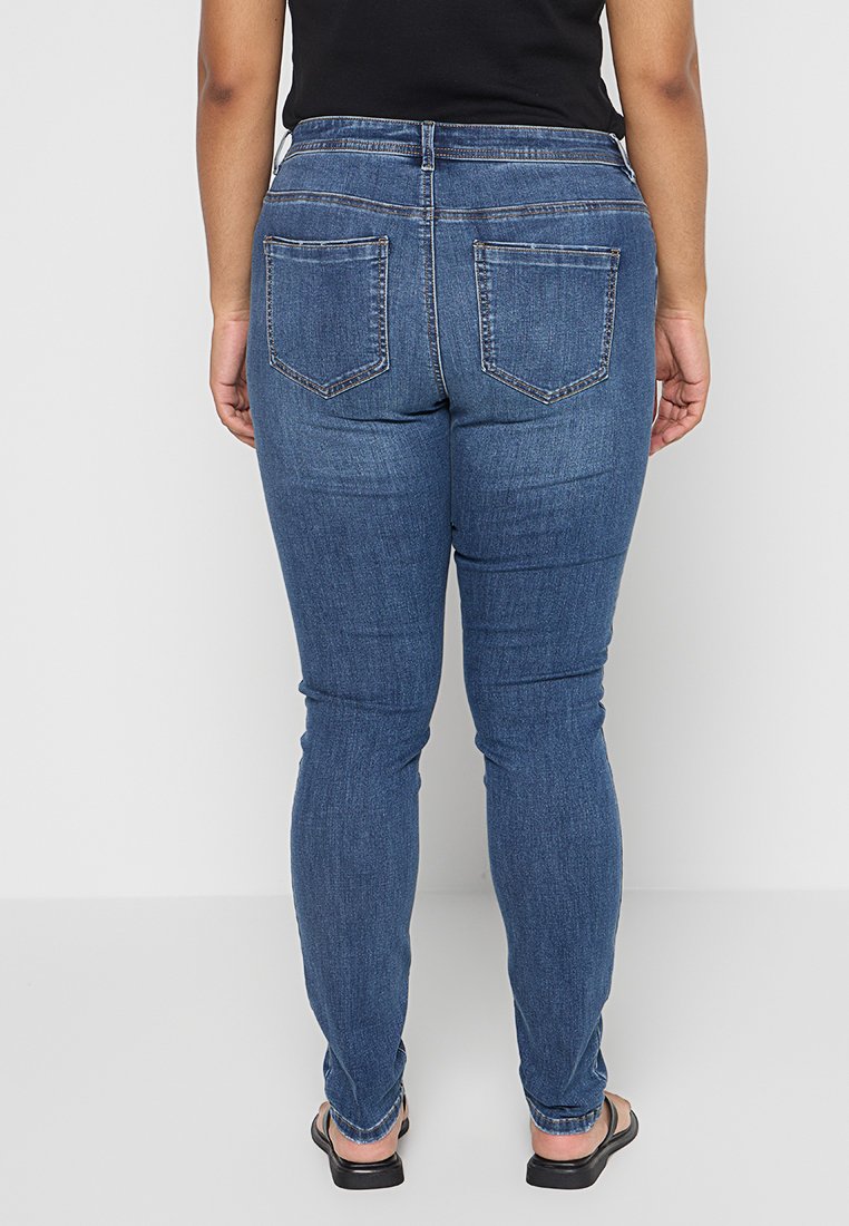 Schlanke Jeans aus dunkelblauem Denim. Mit hoher Taille, Gürtelschlaufen und zwei hinteren Taschen mit einer schlichten Nahtgestaltung. Glatte Textur.