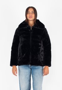 Giacca in pelliccia sintetica nera con zip frontale, colletto alto e maniche lunghe. Tessuto morbido e vestibilità comoda, abbinata a jeans blu chiaro.