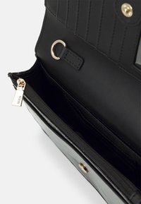 Svart plånbok i konstläder med horisontella ränder, ett blixtlåsförsett fack och detaljer i guldton.