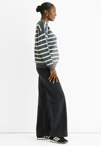 Gray and white striped knitted sweater, black wide-leg jeans, and black sneakers with white accents. Focus on light texture and contrasting colors.