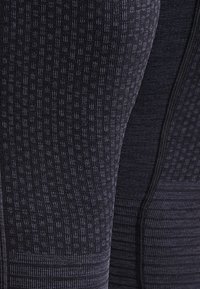 Svarta leggings med texturerade mönster, som har en slät yta och sömmar. Tyget verkar vara stretchigt och figursytt.