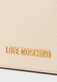 Μπεζ υφασμάτινη επιφάνεια δέρματος με ανάγλυφα χρυσά μεταλλικά γράμματα της μάρκας "LOVE MOSCHINO".