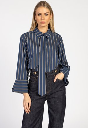 Marine gestreepte blouse met een striknek, lange uitlopende mouwen en contrasterende lichte strepen. Gecombineerd met hoge taille donkere spijkerbroek.