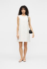 Αμάνικο ανοιχτό μπεζ φόρεμα με υφασμάτινο μοτίβο, συνδυασμένο με ροζ μπαλαρίνες και μια μικρή μαύρη τσάντα.