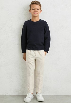 Marineblauer Strickpullover, cremefarbene Hose mit geradem Schnitt und weiße Turnschuhe. Einfaches Design mit gerippten Bündchen und Bund.