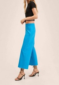 Pantalons larges bleus en tissu lisse, associés à un haut court ajusté noir et des sandales à talons hauts noires à lanières.