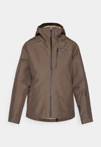 Giacca impermeabile marrone con cappuccio, chiusura frontale con zip, due tasche laterali e polsini regolabili. Presenta un patch con il logo sul petto.