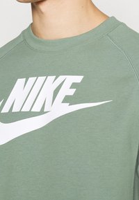 Světle zelená mikina s velkým bílým logem Nike na hrudi. Vyrobena z měkkého materiálu s vroubkovaným výstřihem a raglánovými rukávy.