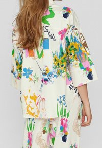 Overdreven shirt van crème stof met levendige bloemen- en abstracte patronen. Heeft verlaagde schouders en een losse pasvorm met opgerolde mouwen.